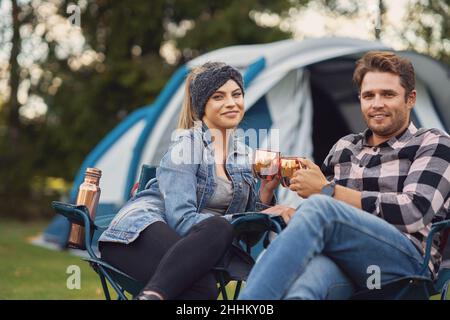 Young nice couple sitting on chairs inf front of tent on camping Stock Photo