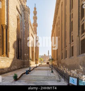 Pedestrian passage separating Royal era Mosque of Al Rifai and Mamluk era Mosque and Madrassa of Sultan Hassan, with facade of Mosque of Qanibay AlRamah at the far end, Old Cairo, Egypt Stock Photo