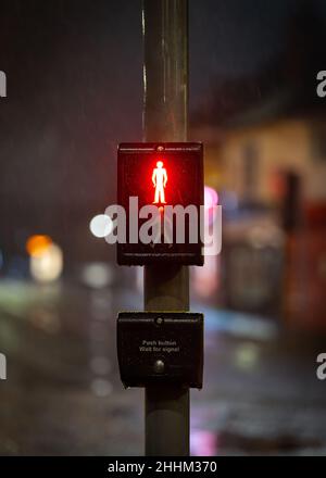 Red man stop sign illuminated at night on traffic light zebra crossing with road and streetlights out of focus behind. Pedestrians waiting for green Stock Photo