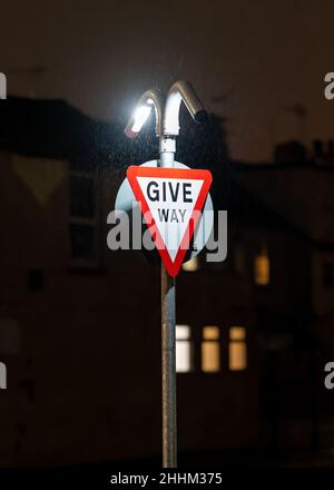 Give way traffic sign brightly illuminated at night in dark. LED lights shining on triangle signage warning traffic of bust junction in darkness. Stock Photo