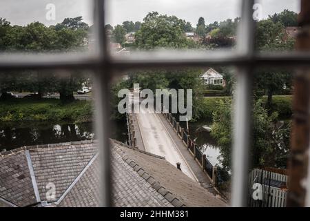 Old historic road bridge crossing river viewed through window from high angle.  Looking out of window from building. Stock Photo