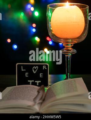 A slate with the word "letter" appears to come out of a book, with a lit candle next to it and bokeh lights in the background Stock Photo
