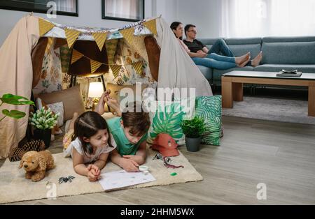 Children playing camping at home while their parents watch TV Stock Photo