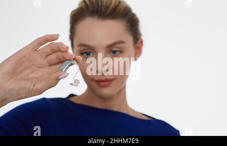 Treatment of deafness in adult people, hearing solutions. Beautiful woman holding latest generation hearing aid in her hand on foreground Stock Photo