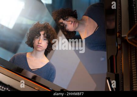 Young woman with curly hair sitting at a grand piano thinking and playing Stock Photo