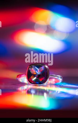 Cushion cut amethyst silver ring on rainbow neon light background with light leaks and bokeh. Artistic jewellery presentation in vivid colors Stock Photo