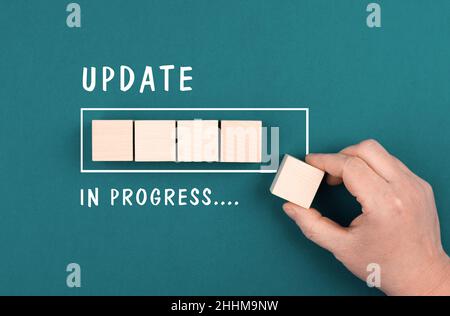 The words update in progress are standing beside the loading bar, hand puts last cube to the upload, petrol colored background Stock Photo