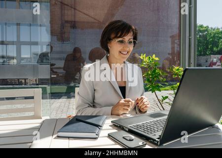 Senior businesswoman in white blazer work in cafe. Remote work. Stock Photo