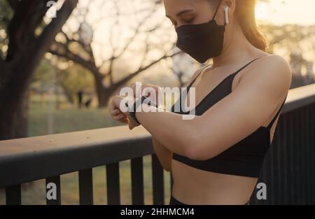 Woman wearing a protective mask and setting up the fitness smart watch for running. Sportswoman checking watch device. Stock Photo