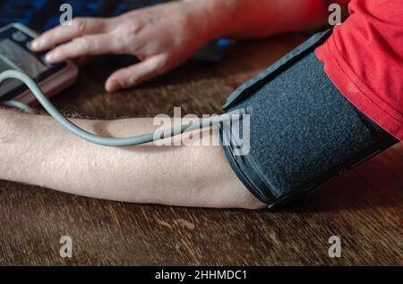 Close-up of a man's shoulder with a blood pressure cuff on. Adult male presses button to turn on digital blood pressure monitor. Measuring blood press Stock Photo