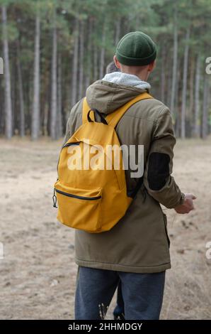 View from the back of a young man with a yellow backpack. The male is standing in front of tall conifers. Hiking. Selective focus Stock Photo