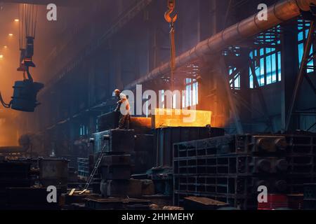 Metallurgy plant interior. Foundry worker on big mold for iron cast. Heavy industry. Steel factory. Stock Photo