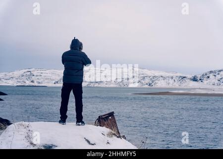 enjoys the views of the empty sandy winter sea, in a winter jacket walks forward along the beach Stock Photo