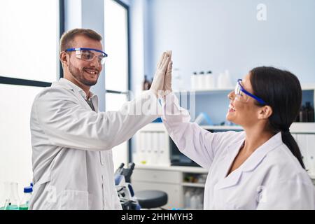 Man and woman scientist partners high five with hands raised up at laboratory Stock Photo