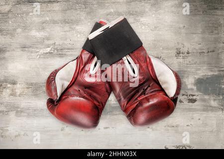Pair of vintage boxing gloves of red and white leather, with black elastic rubber wrist strap, placed over grunge grey background Stock Photo