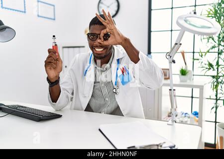 Young african american doctor man holding electronic cigarette at medical clinic smiling happy doing ok sign with hand on eye looking through fingers Stock Photo