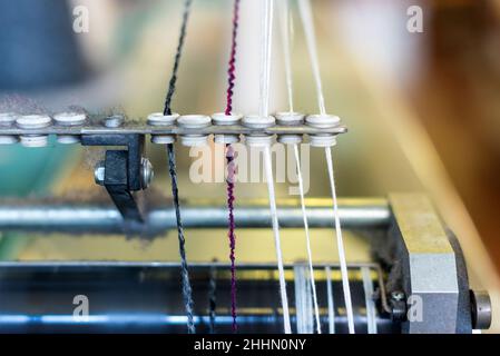 Close up detail on a yarn feeder on a commercial knitting machine with assorted colored threads of cashmere wool threaded through the guides in a knit Stock Photo