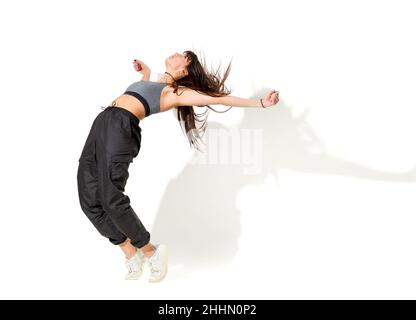 Full body of slim young female hip hop dancer in sportswear performing dance movement in white studio Stock Photo