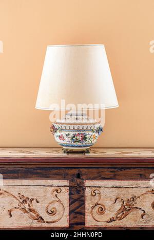 Old fashioned lamp with light lampshade placed on ornamental wooden cabinet against beige wall Stock Photo