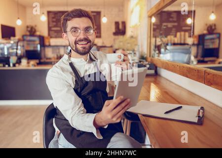 Joyful man drinking coffee and using tablet computer in cafe Stock Photo