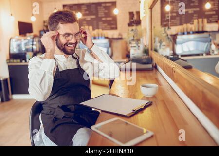 Cheerful male barista putting on glasses in cafe Stock Photo