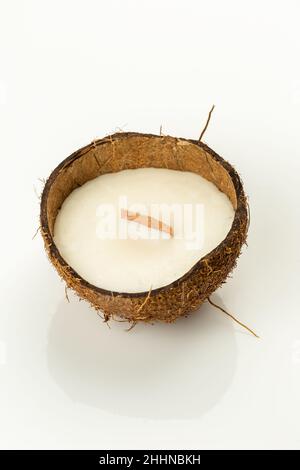 Decorative natural soy wax candle in a coconut shell with wooden candle wick on white glossy surfase. Reuse DIY idea Stock Photo