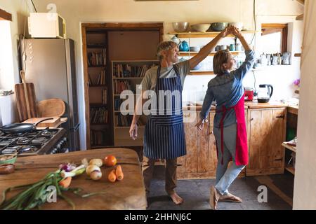Mature caucasian couple dancing while cooking food together in kitchen at home. simple living, togetherness, lifestyle and love. Stock Photo