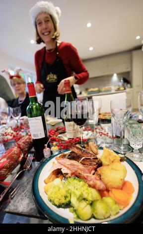 Christmas dinner UK; a woman with a santa hat on serving a plate of christmas lunch on a table at Xmas; UK Stock Photo