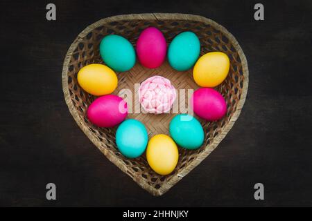 Easter eggs in weaved basket on black background. a basket made of straw in the form of a heart with colorful eggs painted for the holy orthodox Chris Stock Photo