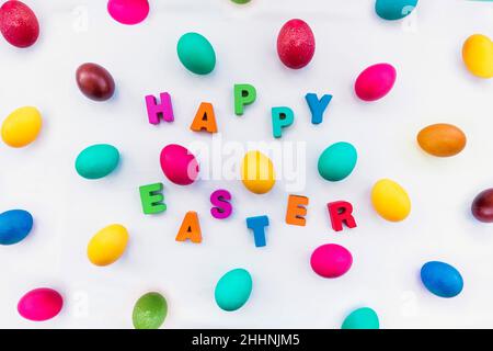 Lots of colorful eggs and the inscription happy Easter on a light tablecloth. The concept of the celebration of Easter Sunday in the Christian traditi Stock Photo