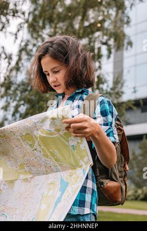 Hipster young girl looks at the map. Cute brunette teen girl travels in summer vacation. Vertical shot Stock Photo