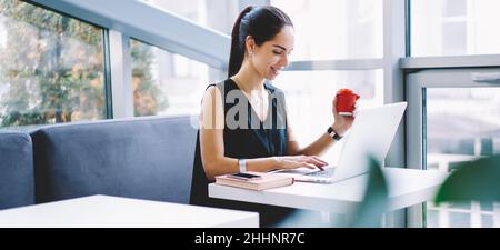 Cheerful female remote worker using laptop in cafe Stock Photo