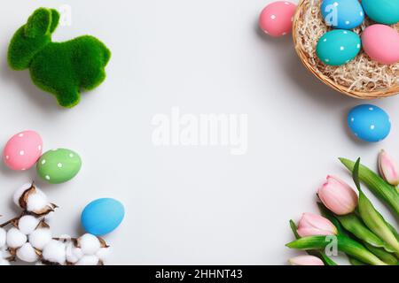 Easter composition. Multi-colored eggs in a basket, tulips rabbit flowers on a gray background. Flat lay top view copy space for greeting cards. Stock Photo