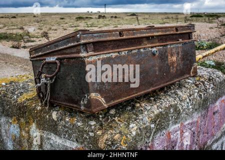 Close-up of a rusty old disheveled large metal box found on a concrete wall, with Dungeness beach in the background, taken on 14th November 2021 Stock Photo