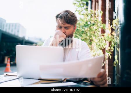 Thoughtful man working on project with documents and laptop Stock Photo
