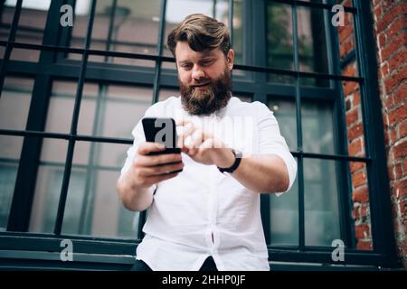 Serious bearded remote worker surfing smartphone on street Stock Photo