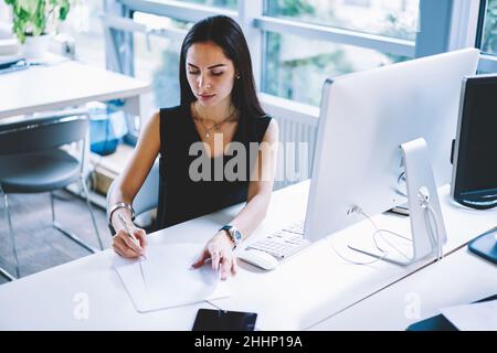 Pensive businesswoman writing notes on paper in office Stock Photo