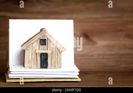 Miniature house placed on a small open book with blank pages against a wooden background. Household manual for the home or estate. Stock Photo