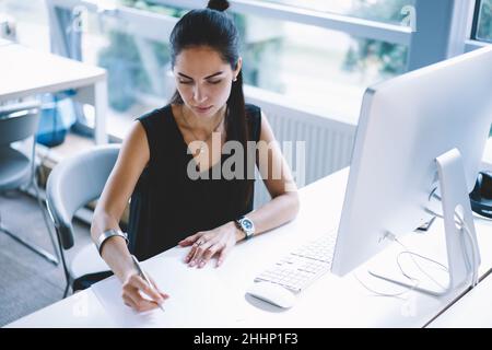 Businesswoman taking notes while working in modern workspace Stock Photo