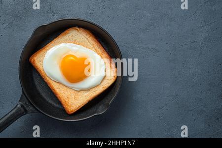 Fried eggs with a heart-shaped yolk on toast in a frying pan. Stock Photo