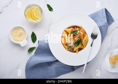 Bolognese Penne Pasta. Tasty appetizing classic italian penne pasta with parmesan cheese, basil and Bolognese sauce in white plate on stone table. Tra Stock Photo