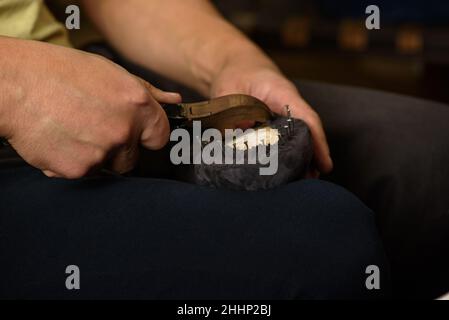 Shoemaker making shoes sitting in workshop. Bootmaker fixing gray suede boot on shoe last with nails and pliers. Closeup Stock Photo