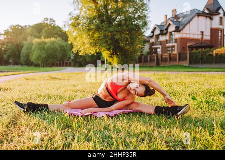 Happy fit woman doing stretching warm up exercises on green grass in countryside Stock Photo
