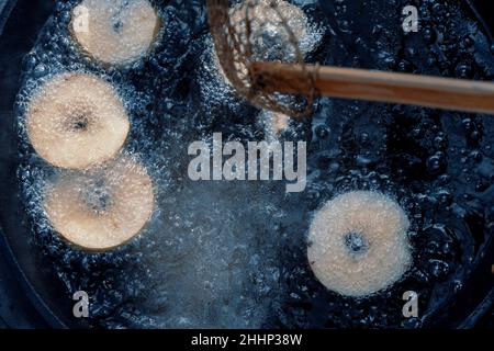 Homemade donuts frying in cast iron skillet outdoors at campsite. Stock Photo