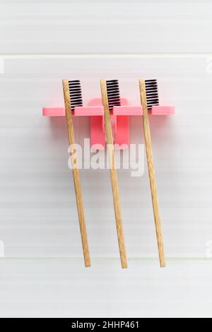 Three natural bamboo toothbrushes with black bristles in a holder against a tile background on the bathroom wall above the washbasin. Selective focus. Stock Photo