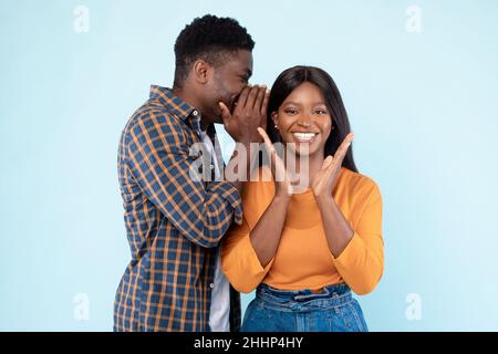 Black man sharing secret with his amazed girlfriend Stock Photo - Alamy