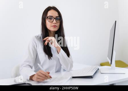 Woman healthcare worker doing some paperwork and using computer while working at doctor's office Stock Photo