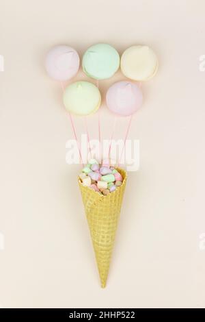 Yellow waffle cone with green, pink and yellow marshmallows looks like macaroons on pastel background Stock Photo