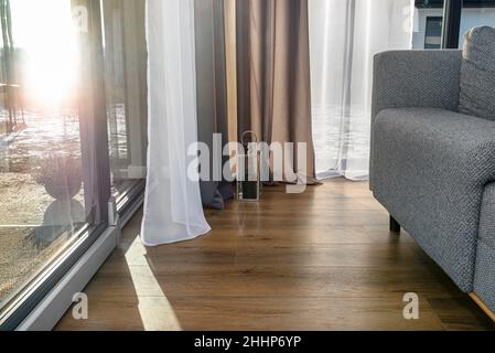 Modern and simple living room in the house with large patio windows and double curtains, a visible gray sofa and a small lantern. Stock Photo