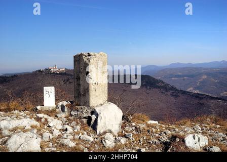 Monte Santo (Skalnica) seen from the crest of the Sabotin. Monte Santo was the theatre of bloody battles during the First World War. The church on the top was razed by the Italian artillery placed on mount Sabotin. It was rebuilt in the years between 1924 and 1928. In the foreground, the pillars of the old border with ex Yugoslavia. Stock Photo